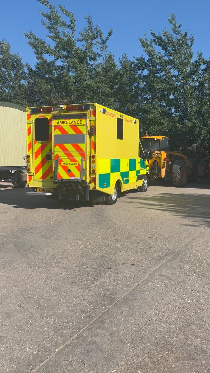 An ambulance with rear doors open in morning sunshine
