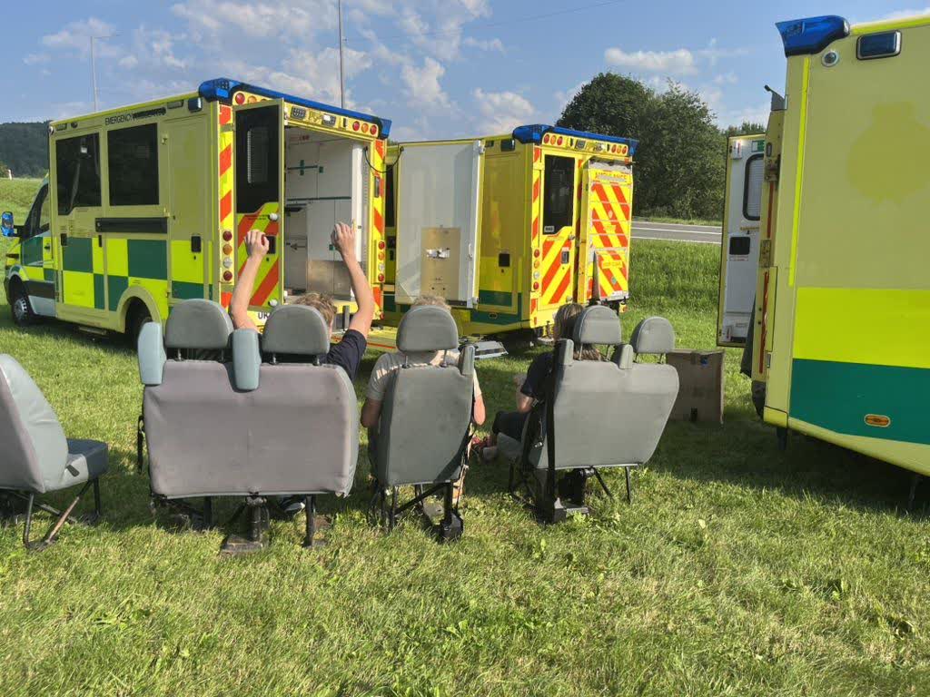 Convoy ambulances pulled over together in a green field, crew resting on removed minibus seats