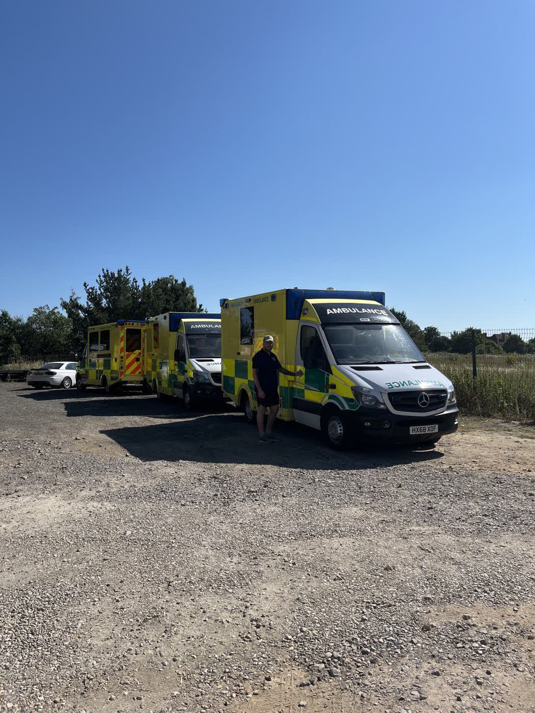 Convoy ambulances parked in a line on a farm yard under a clear blue sky
