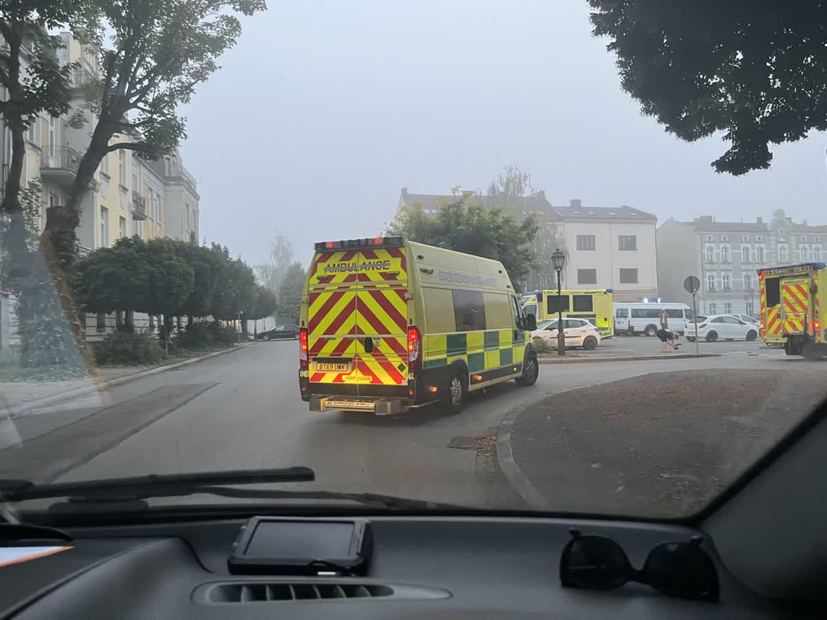 View through a windscreen of convoy ambulances driving through a misty European town square at first light