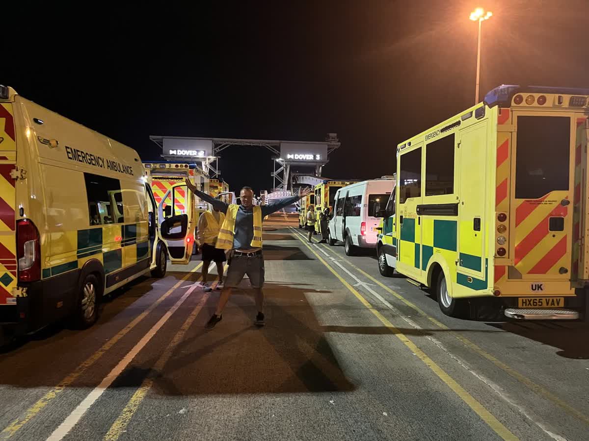 Convoy ambulances lined up at the Dover ferry terminal at night, a volunteer standing between them with his arms raised
