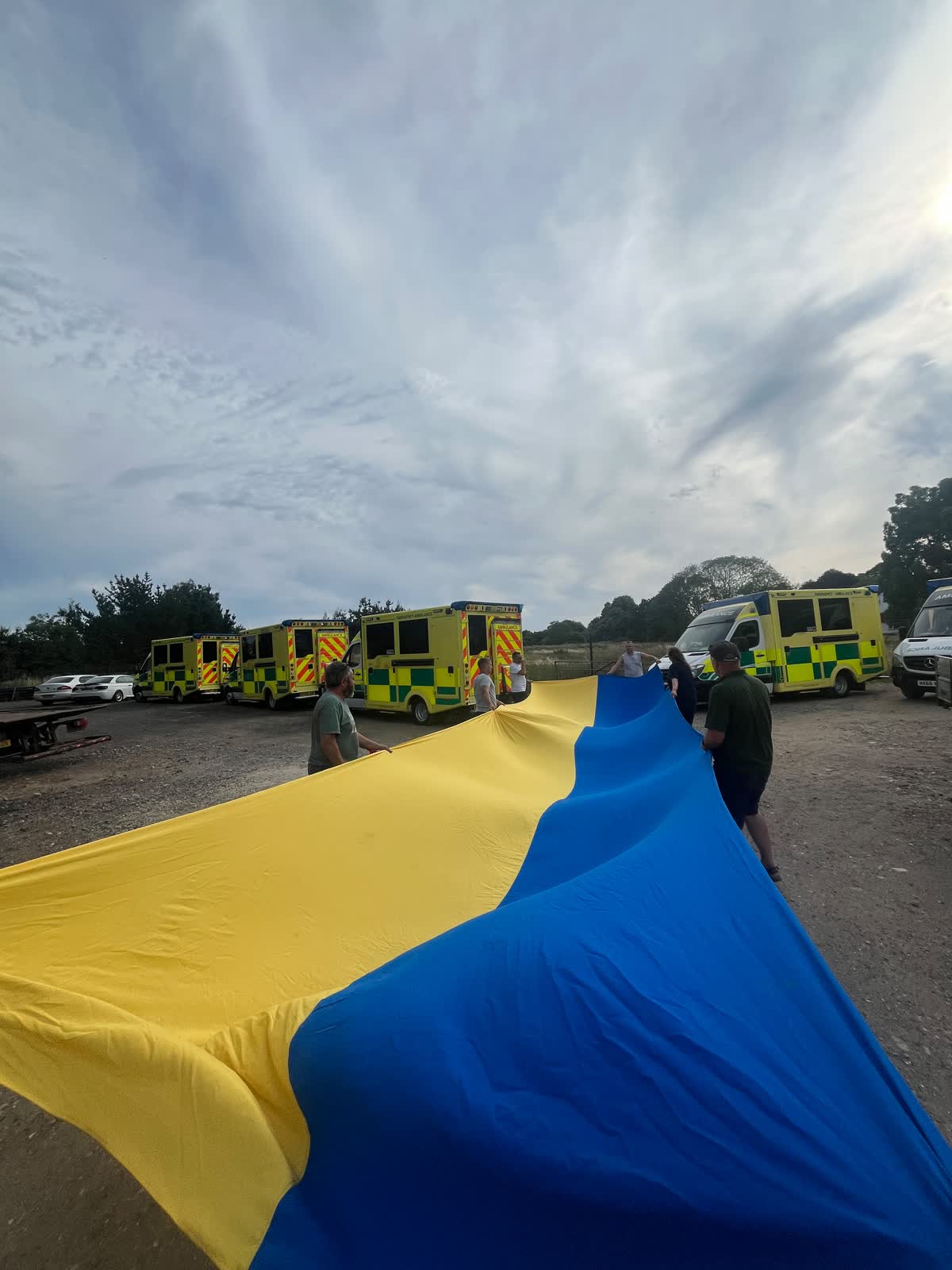 A large Ukrainian flag being unfurled on the yard beside the convoy ambulances