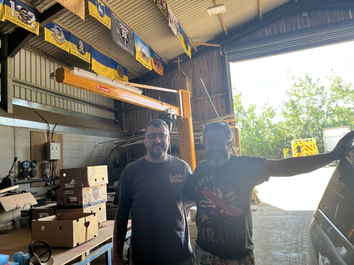 Andrew, left, and James Baird standing together in the loading barn at Church Farm, beneath Ukrainian brigade banners hung from the roof