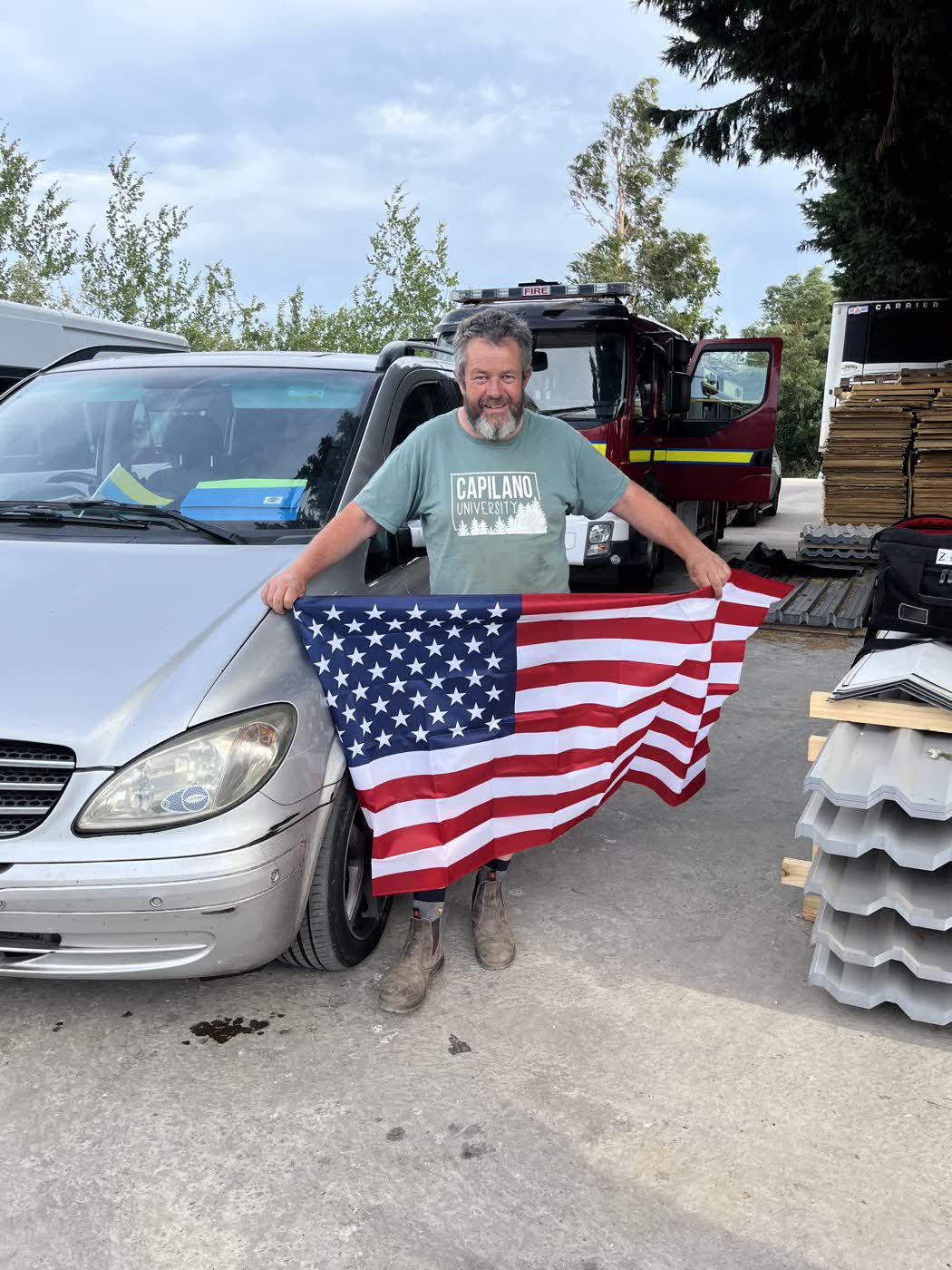 James Baird holding the Stars and Stripes at the farm, beside the convoy vehicles being prepared for Ukraine