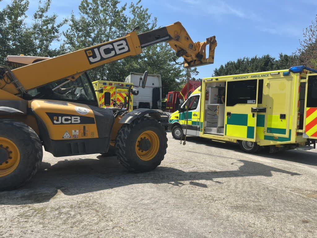 A JCB telehandler loading heavy supplies between convoy ambulances
