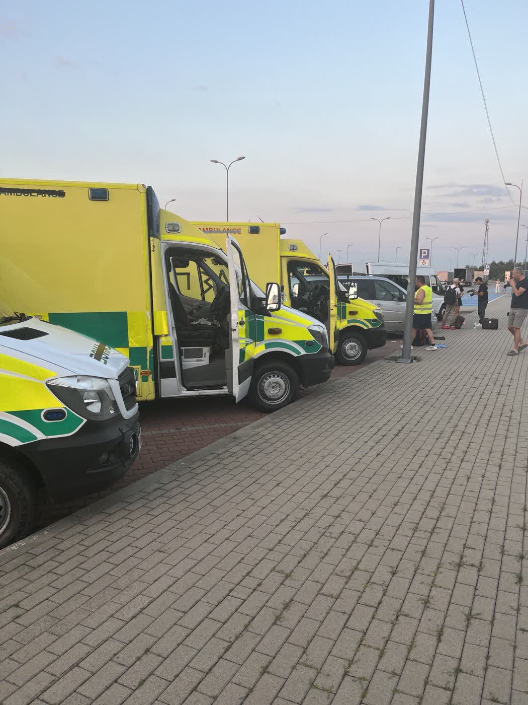 Convoy ambulances with cab doors open at a European service station at dusk, crew standing beside them