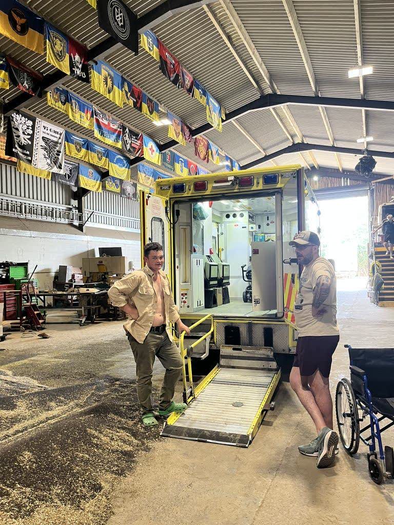 Crew members at the tail-lift of an ambulance inside a warehouse hung with Ukrainian flags and brigade banners