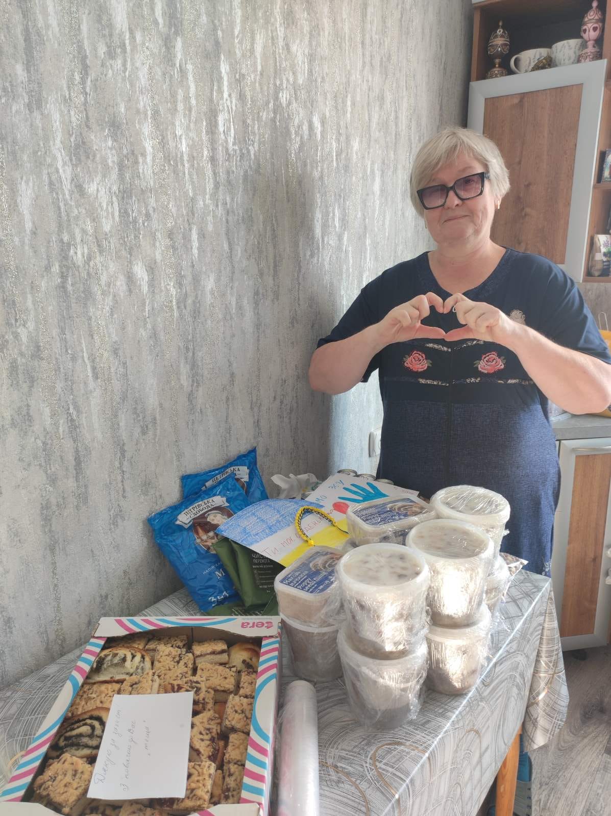 Ukrainian woman making a heart sign with her hands, surrounded by food and aid packages delivered by Medaria Aid